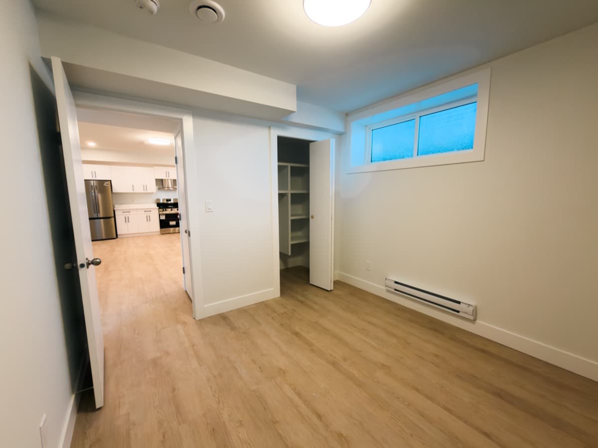 Finished basement bedroom with a window, a baseboard heater, an open closet with shelves and a doorway to the kitchen