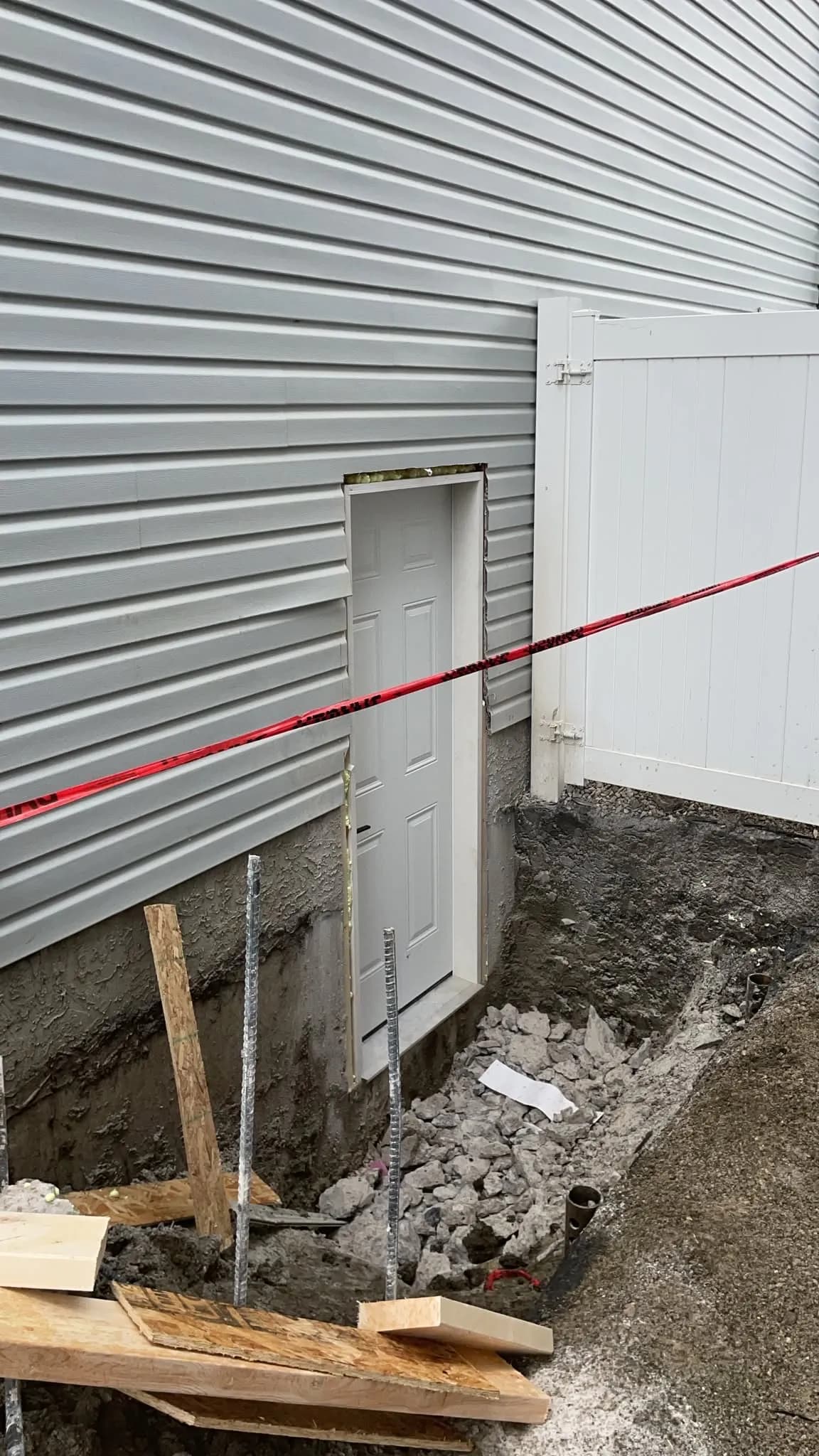 New exterior door set into a cut in a house's foundation wall, with open excavation, gravel and rebar in front
