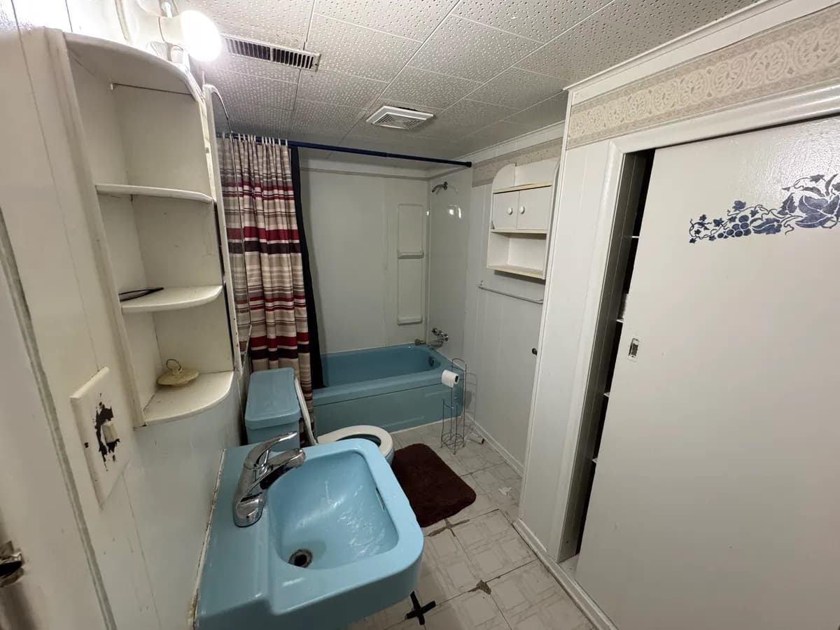 Dated bathroom with a blue tub, blue toilet and blue wall-hung sink, a striped shower curtain and textured ceiling tiles