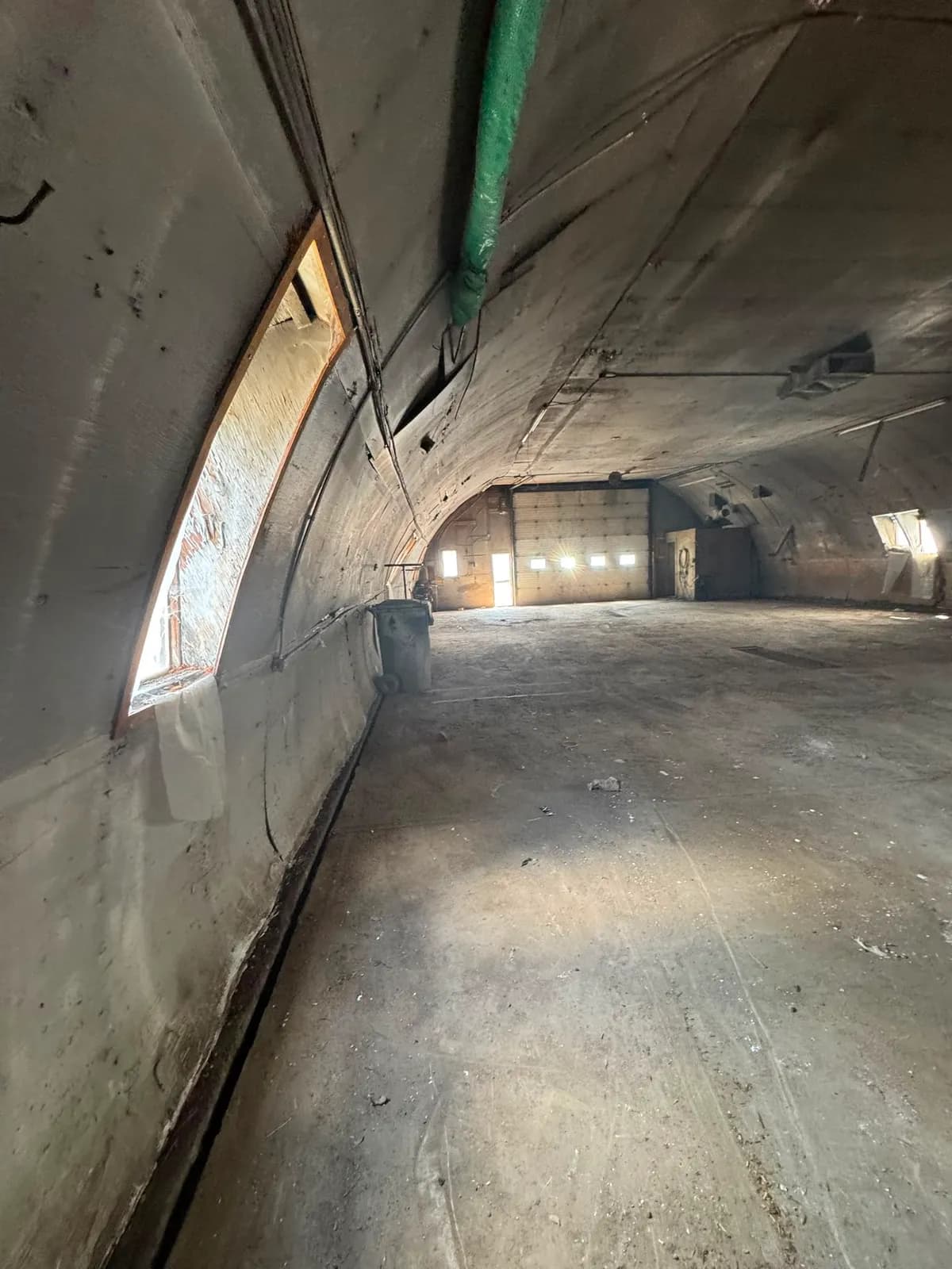 Curved interior wall with a framed window opening, looking down the building toward the overhead door at the far end