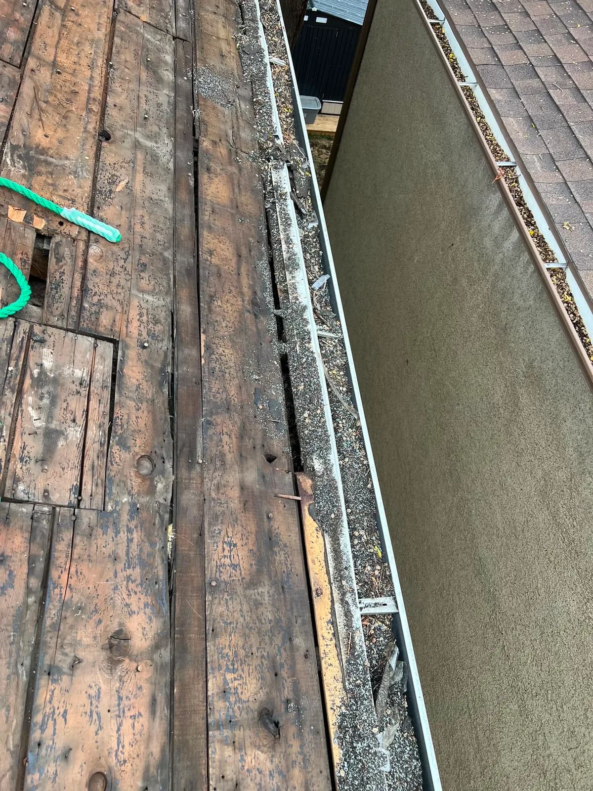 Weathered board decking along the eave with a patched section, next to an eavestrough and the wall below
