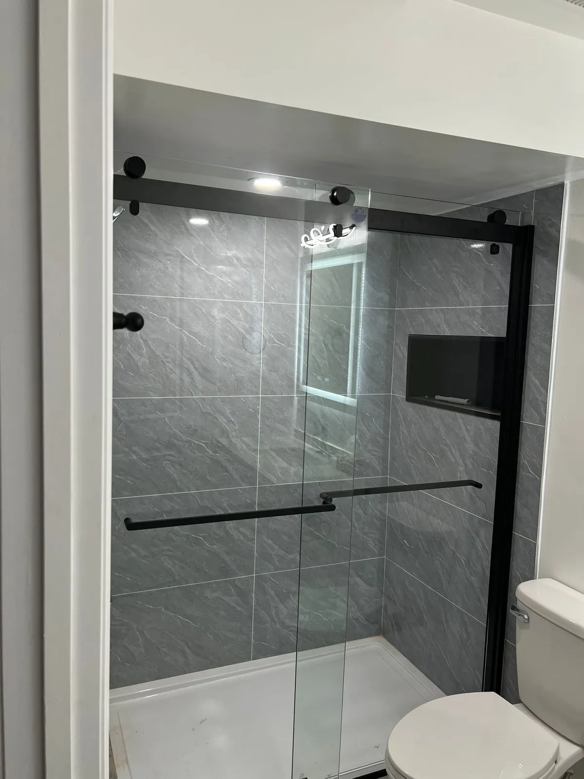Walk-in shower with large grey marble-look tile, a black recessed niche and a sliding glass door with black hardware