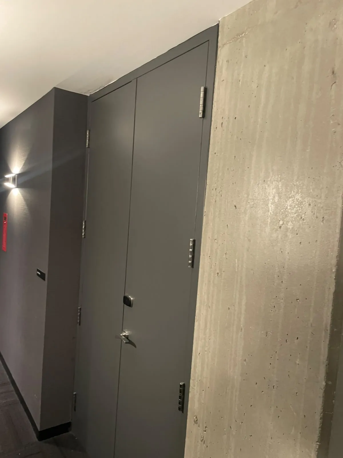 Grey double doors and a wall sconce beside a board-formed concrete wall