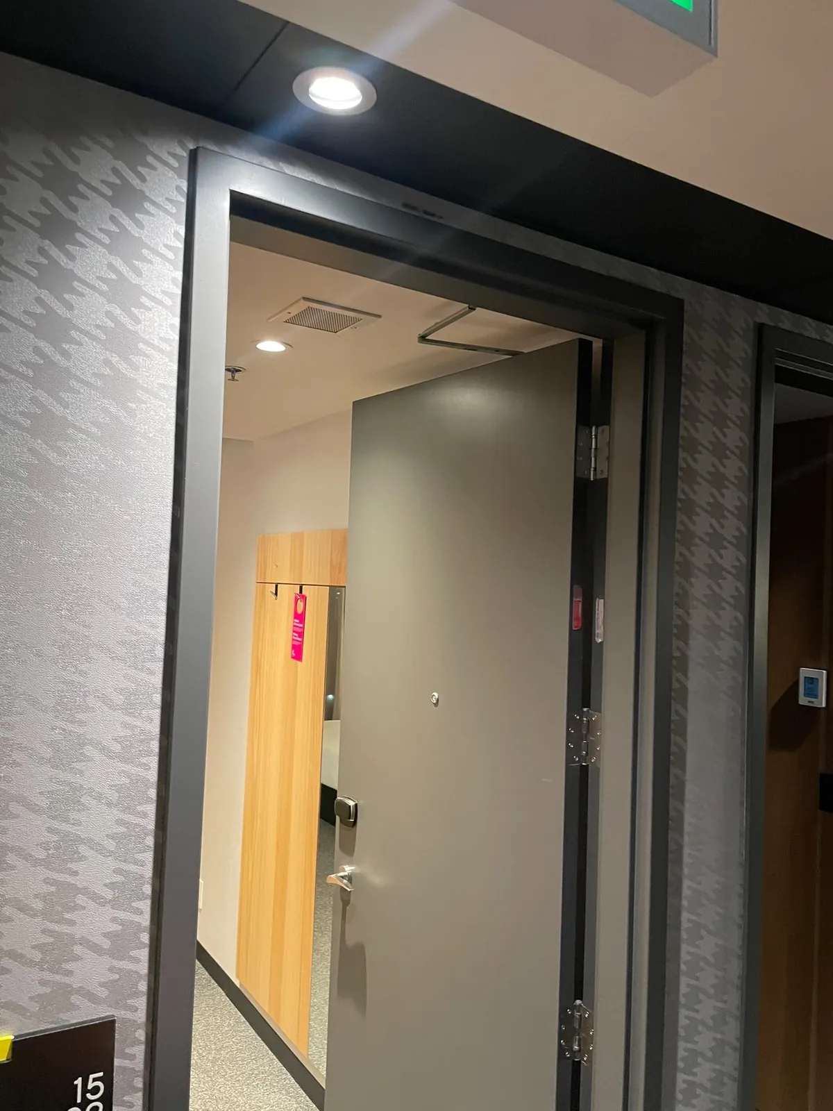 Guest room door open to the room entry, with a recessed light in the dark corridor ceiling