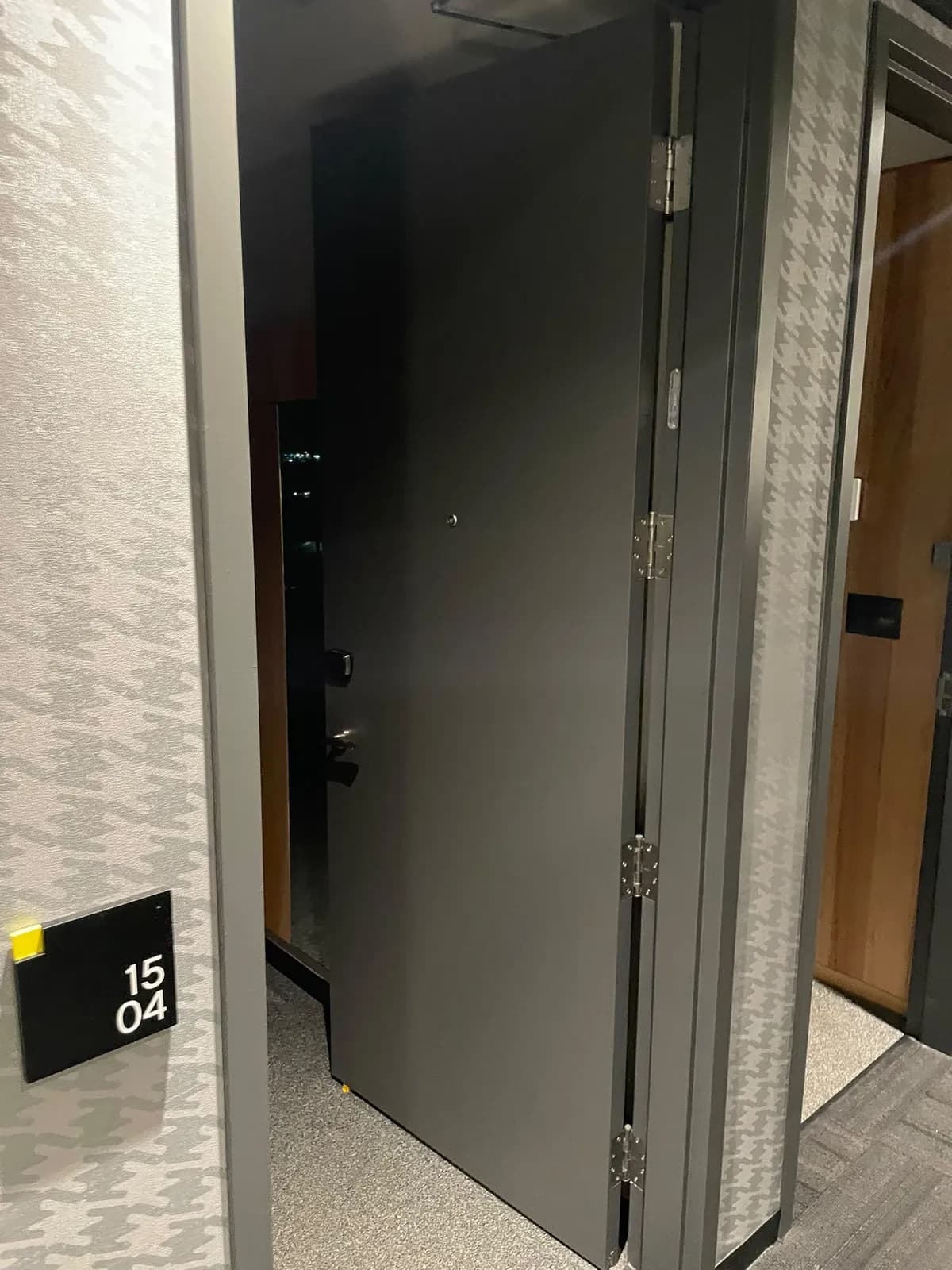 Open grey guest room door next to a room number plaque and houndstooth wallcovering