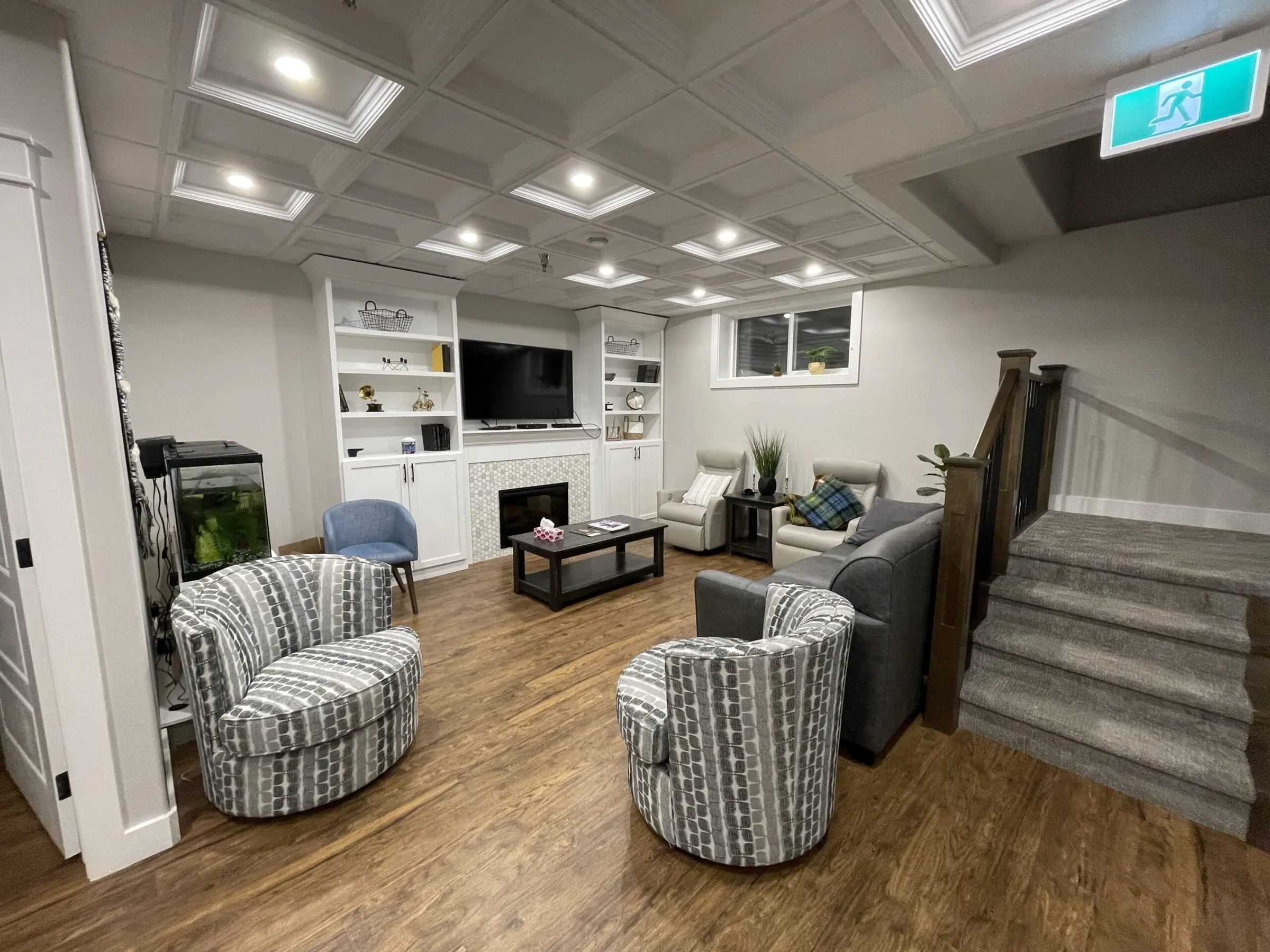 Care home lounge with a coffered ceiling, built-in shelving around a fireplace, swivel armchairs and a carpeted stair
