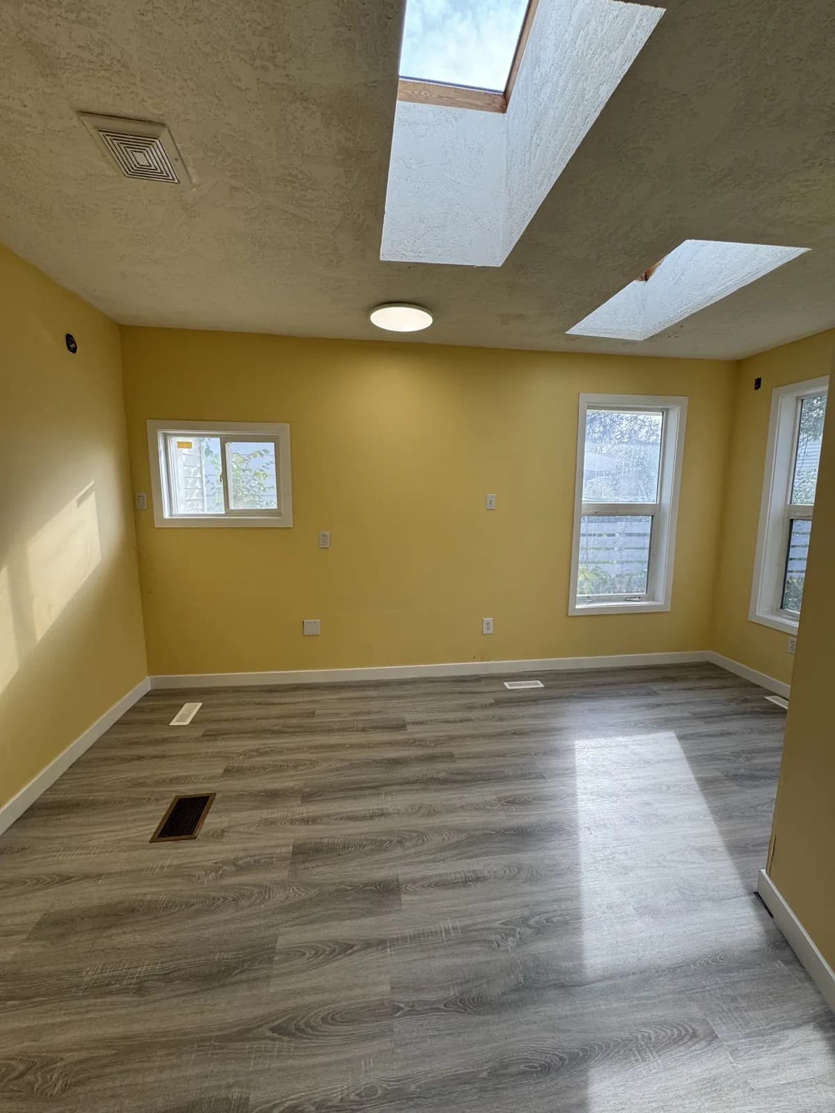Finished addition room with yellow walls, two skylights, three windows and new grey plank flooring