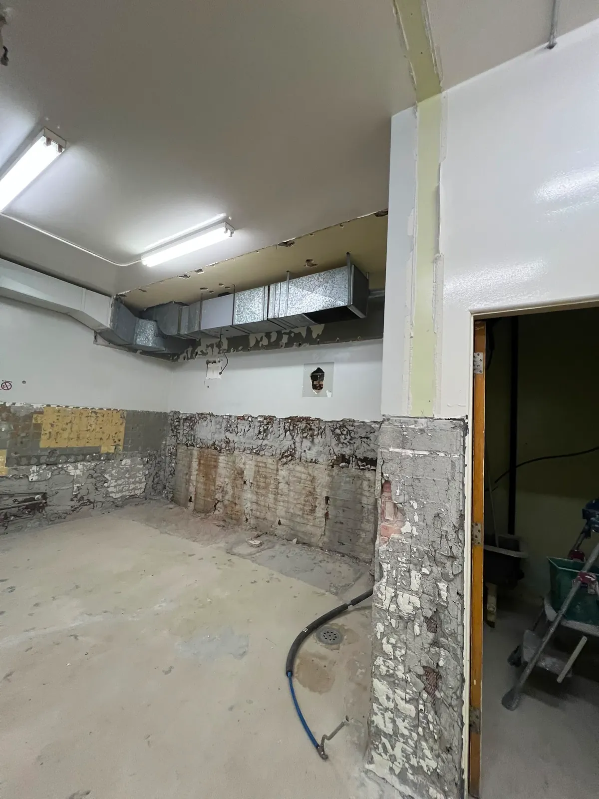 Gutted room with stripped wall tile, exposed ductwork and a doorway to the next room