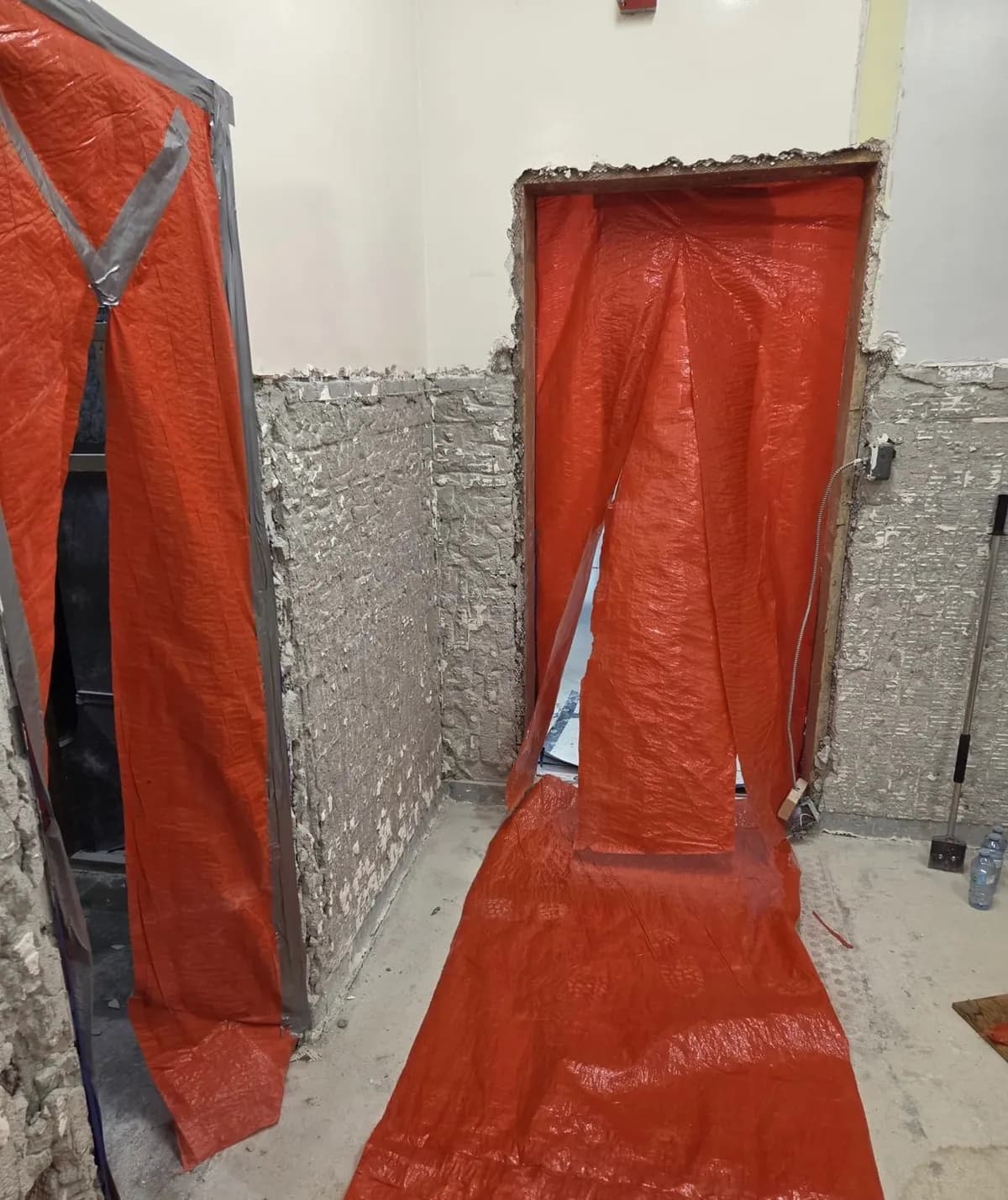 Orange tarp containment hung over two doorways in a room with its wall tile stripped