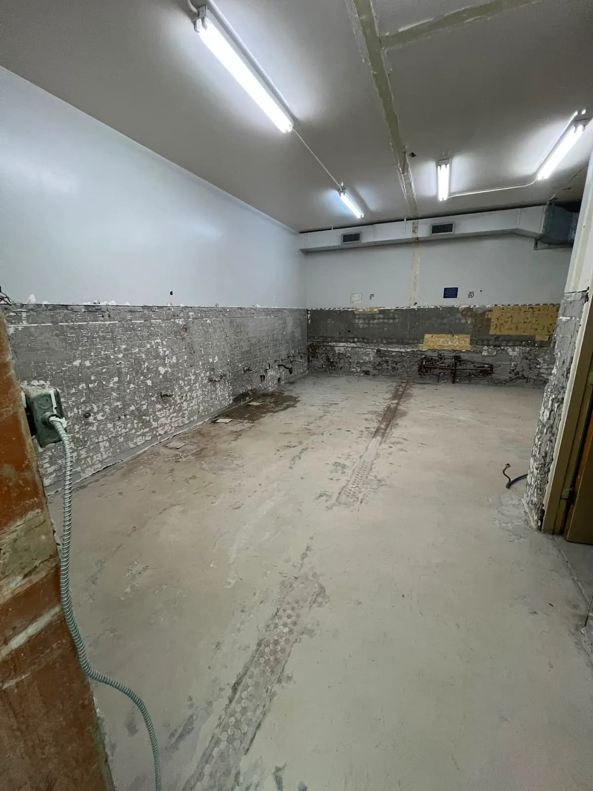 Long room gutted to the floor slab, with tile stripped from the lower walls