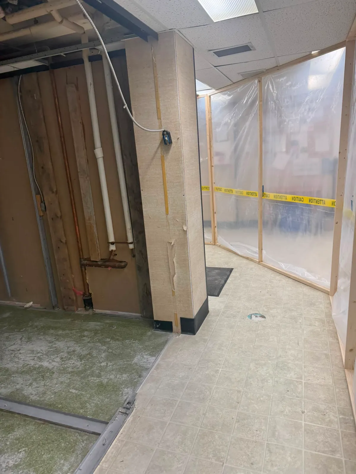 Corridor with new framing on one side and plastic containment with caution tape on the other