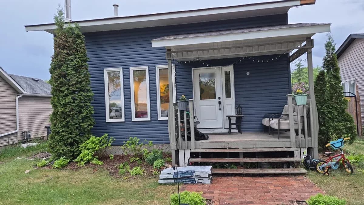 Front of a house with new navy vinyl siding and white trim, siding boxes still stacked on the walk