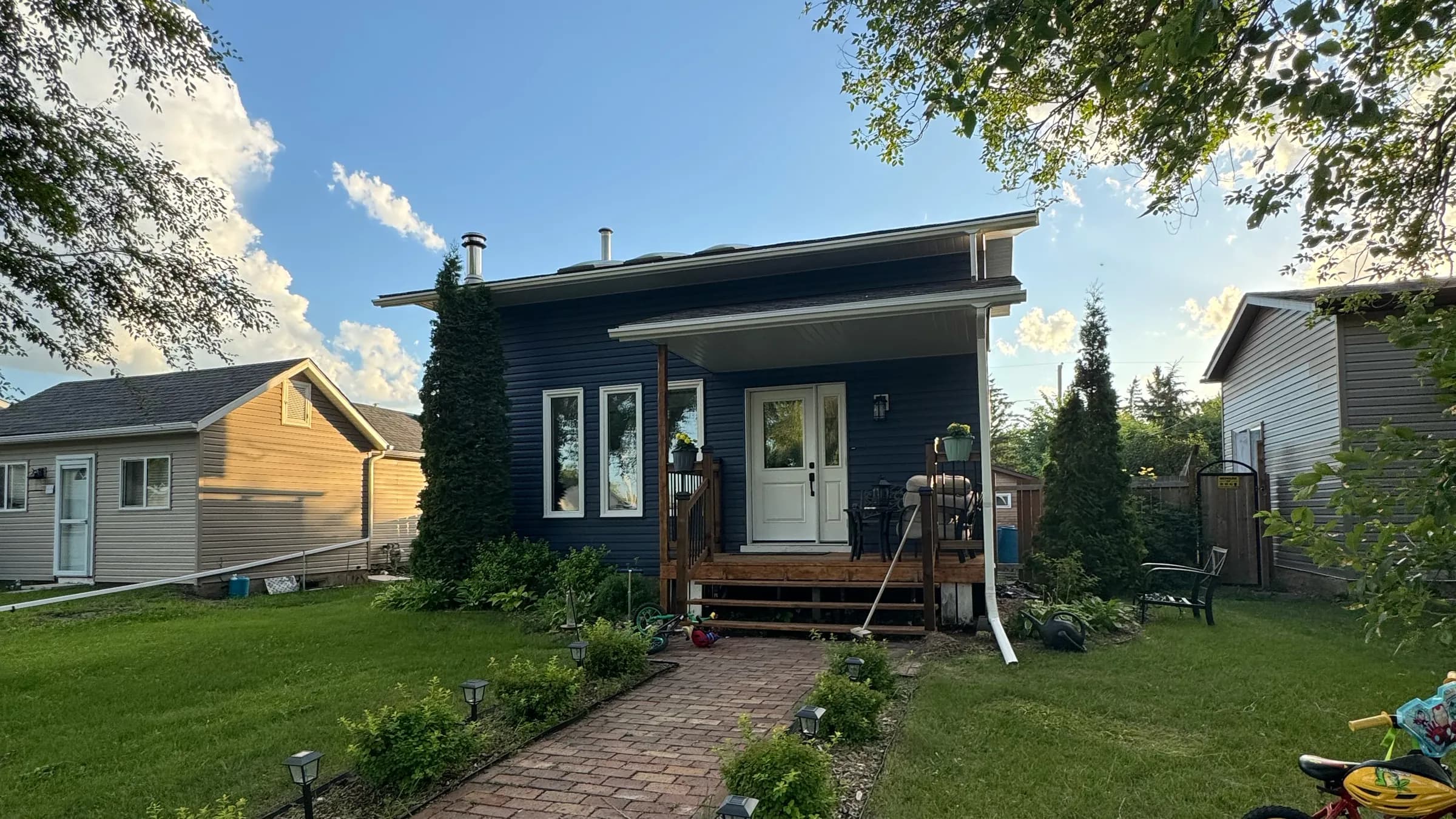 House with new navy vinyl siding, white trim and a stained front porch at the end of a brick paver walk