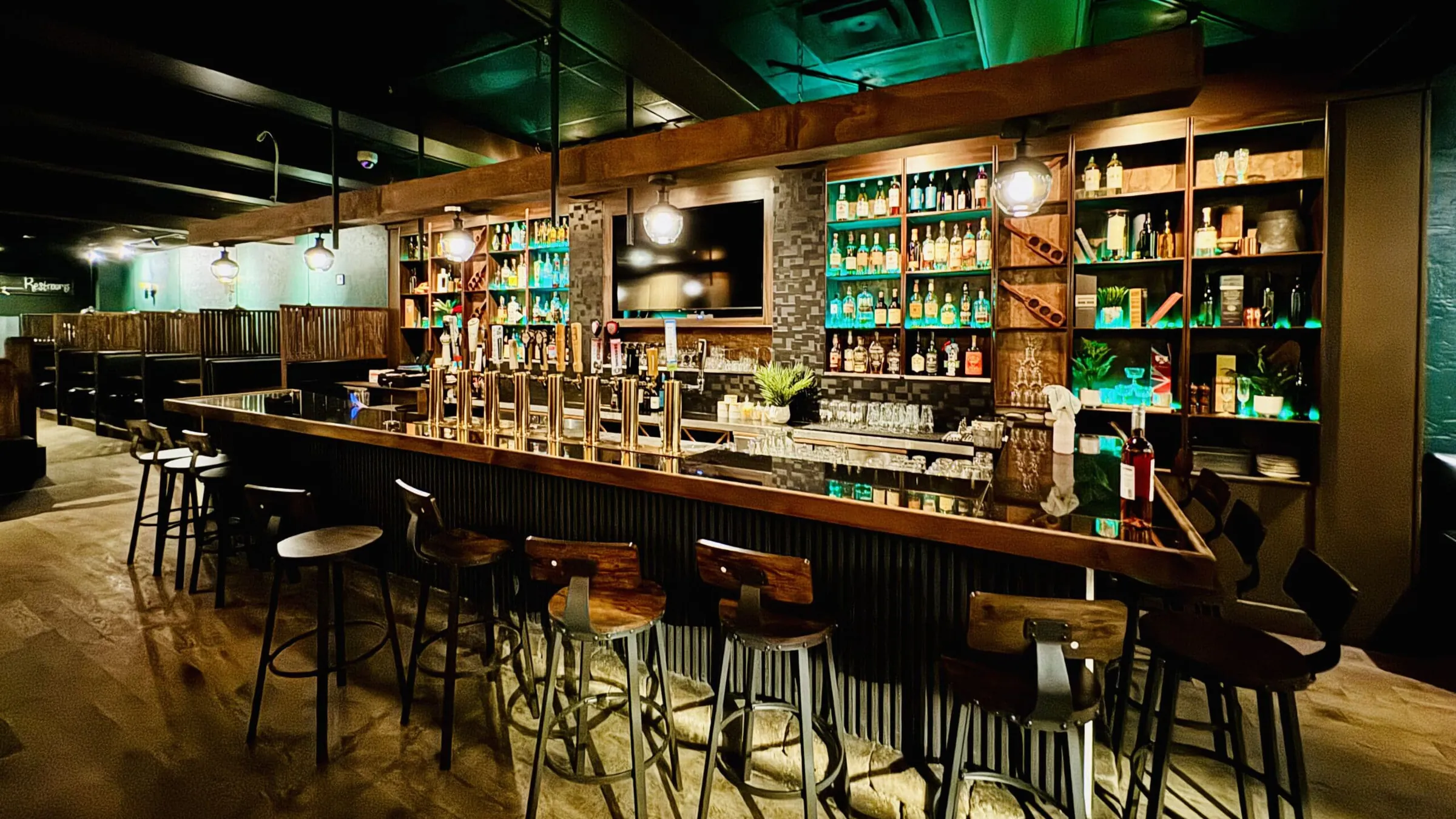 Renovated pub bar with brass beer taps, backlit bottle shelving, pendant lights and wood-seat stools