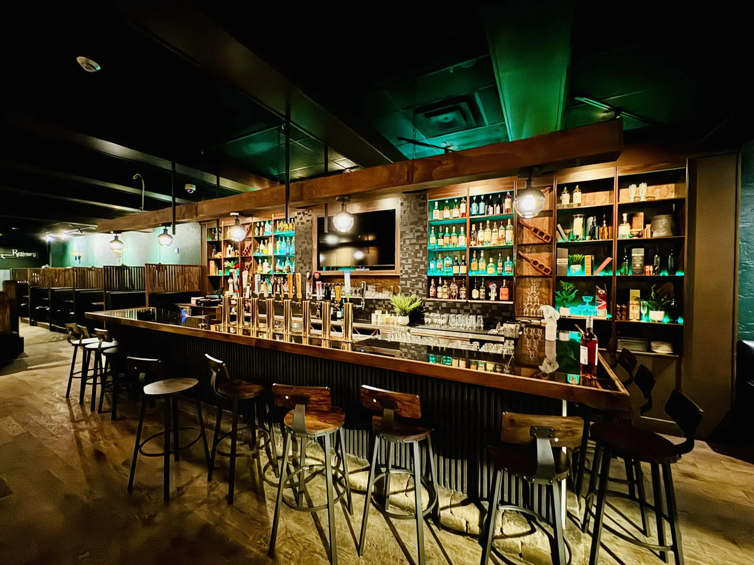 Renovated pub bar with brass beer taps, backlit bottle shelving, pendant lights and wood-seat stools