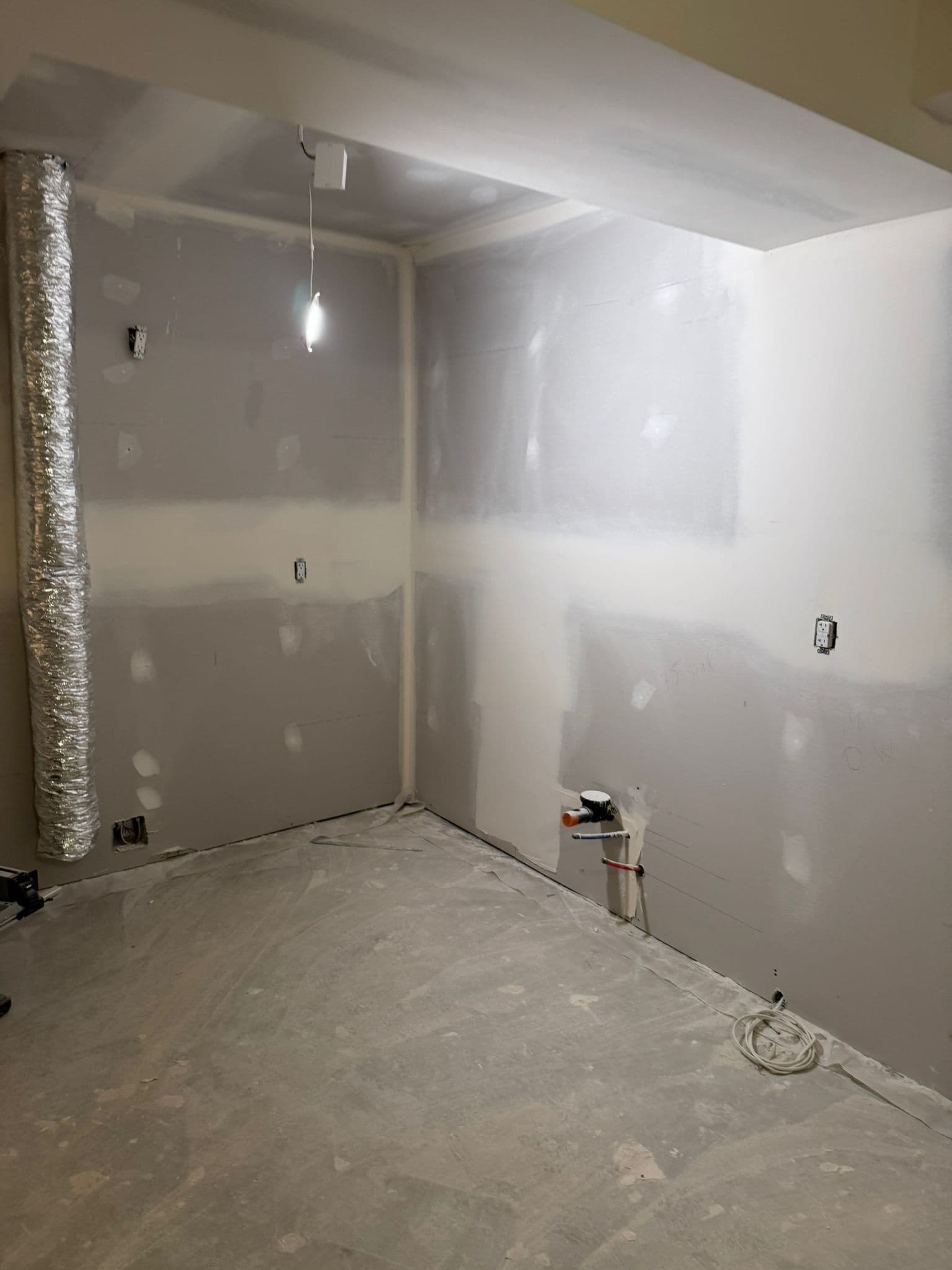 Drywalled basement bathroom with a flexible exhaust duct hanging from the ceiling and a bare concrete floor