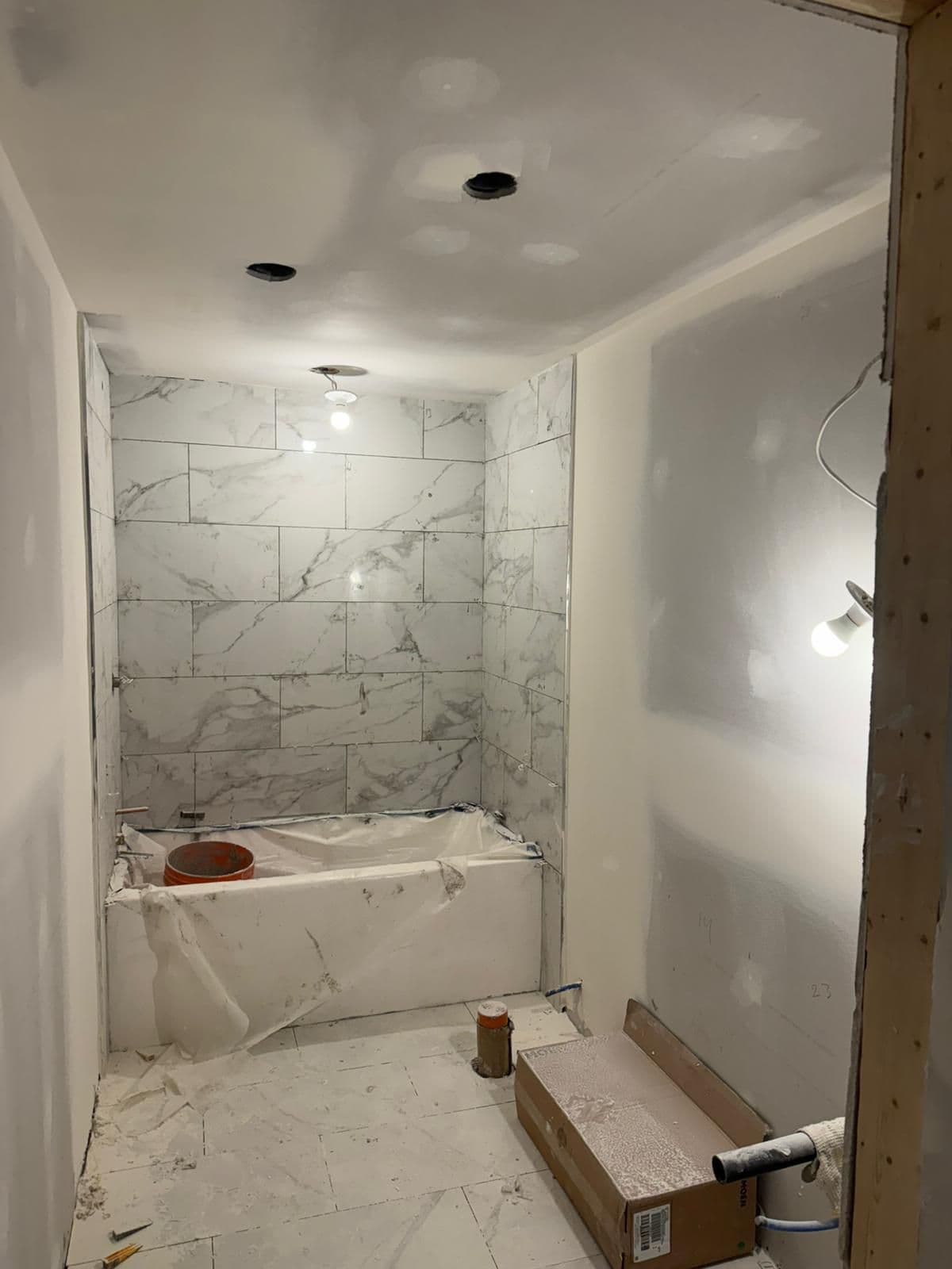 Basement bathroom with marble-look tile around the tub and taped drywall on the walls beside it