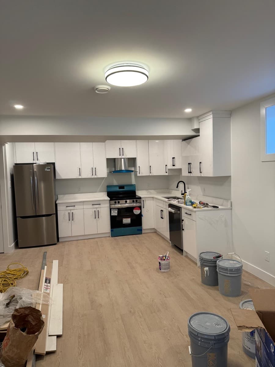 Nearly finished kitchen with counters and sink installed, and paint buckets and trim boards still on the plank floor