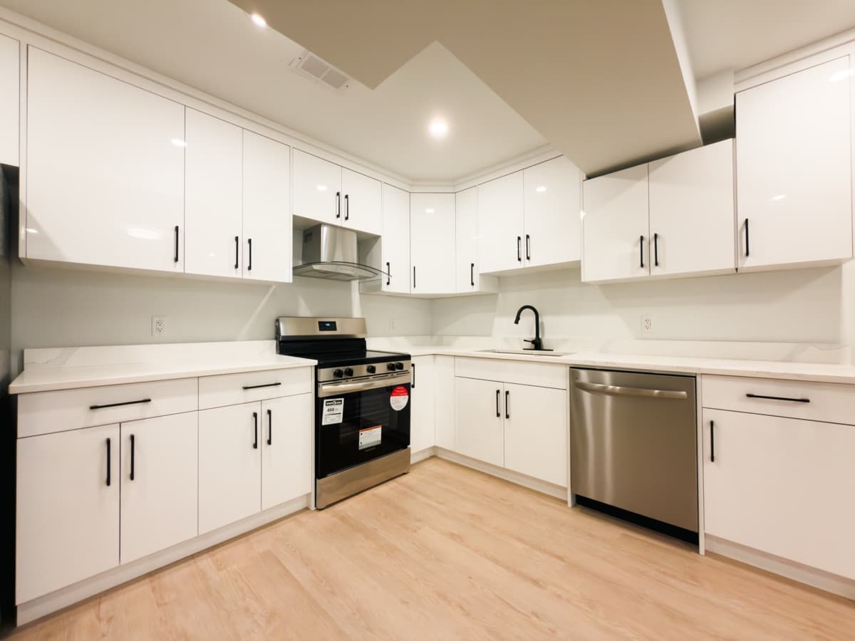 L-shaped white gloss kitchen with black bar pulls, white stone-look counters, a stainless range, chimney hood and dishwasher
