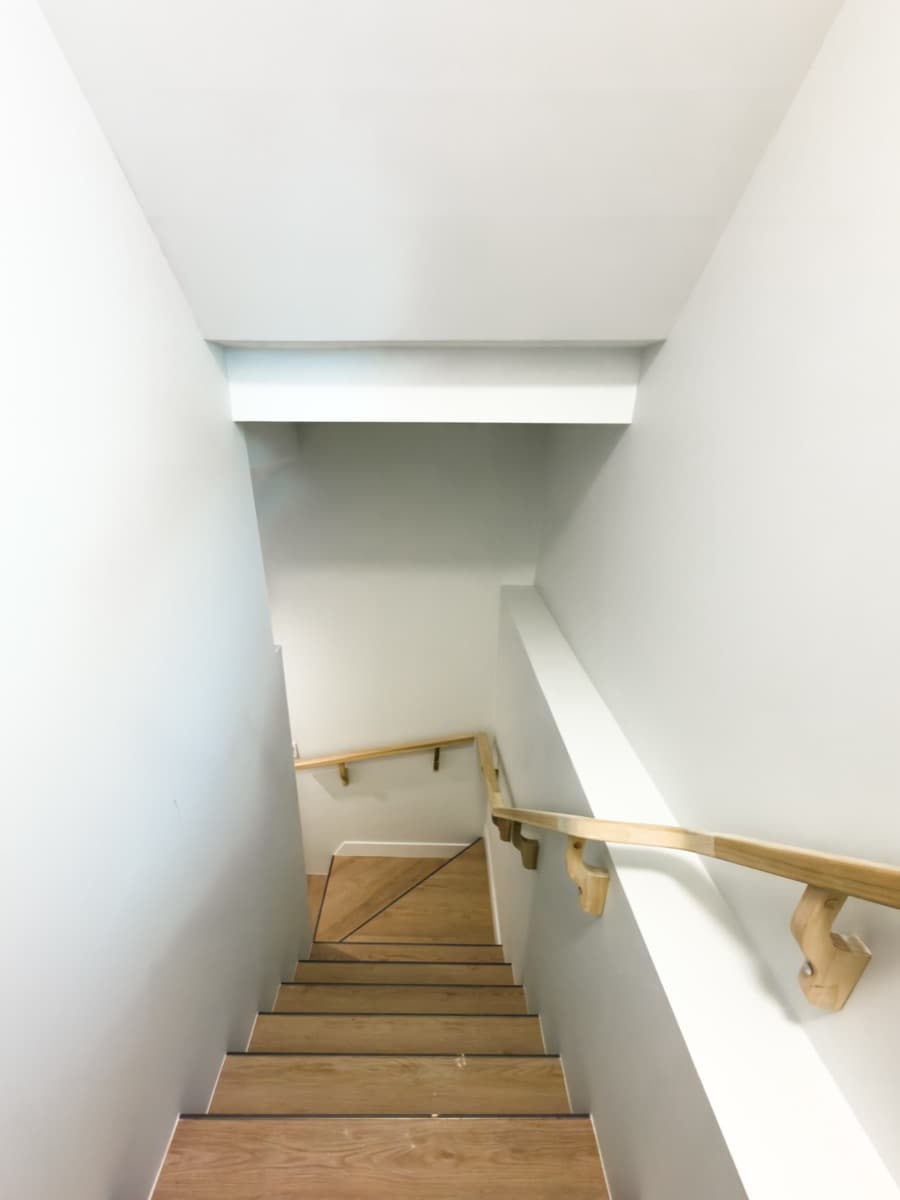 Finished basement stairwell with painted walls, a wooden handrail and plank-covered steps