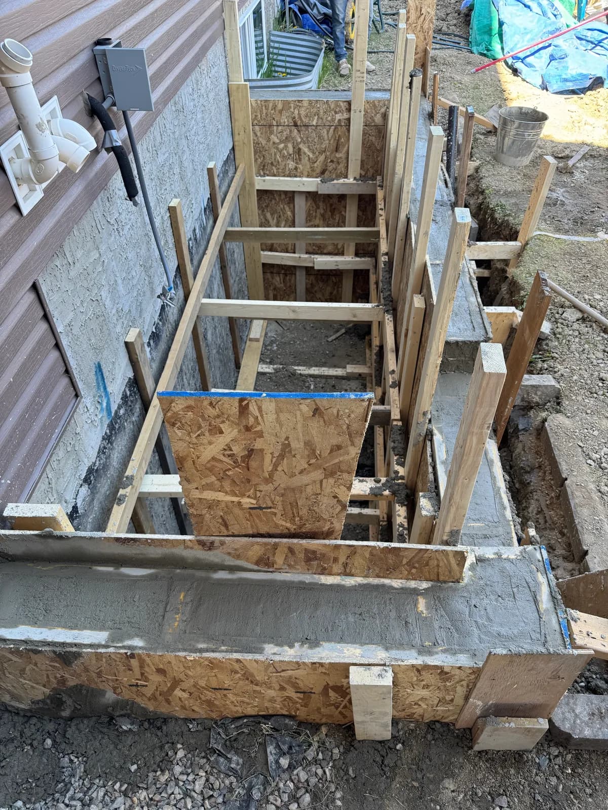 Wood forms and freshly poured concrete for the walls of an exterior stairwell beside a house