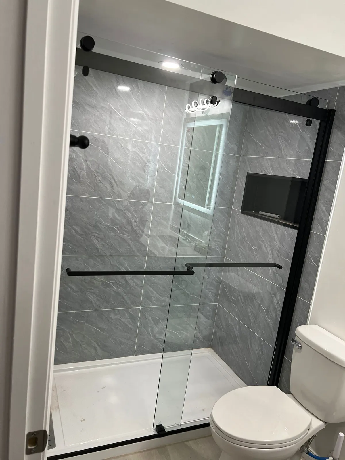 Walk-in shower with a sliding glass door on black hardware, large grey stone-look tile and a recessed niche