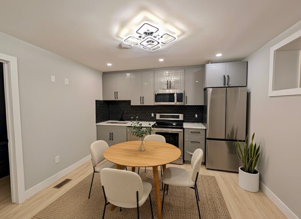 Basement suite with a round wood dining table and white chairs in front of a grey kitchen with a hexagon tile backsplash