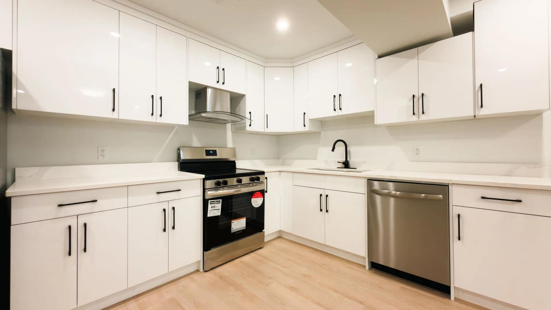 Finished basement suite kitchen with white flat-panel cabinets, quartz counters, stainless appliances and light plank flooring