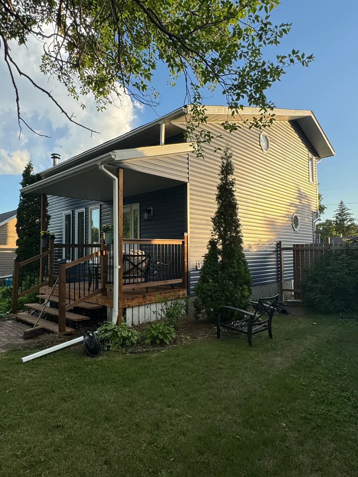 Corner view of a house with new blue vinyl siding, octagon gable windows and a stained wood porch with stairs