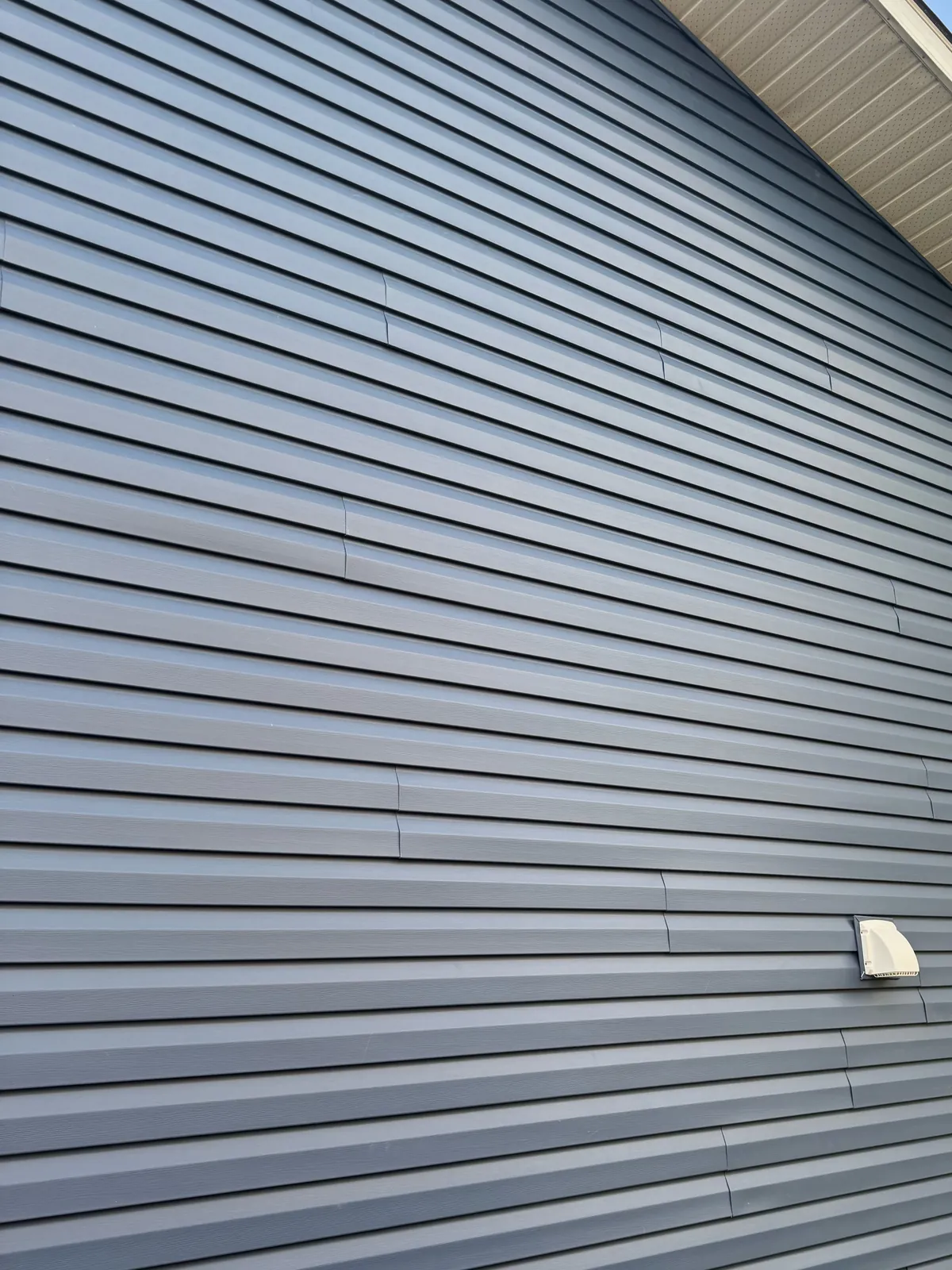 Close view of new blue vinyl siding running up a gable wall to white soffit